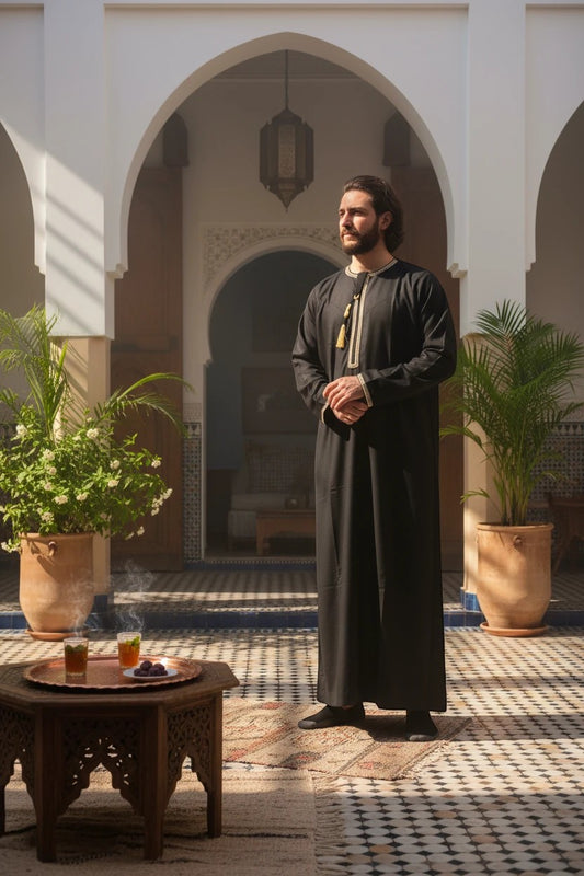 Khayr Thobes traditional black thobe with gold and black embroidery and tassels on the neckline. Long sleeves and flowing silhouette.