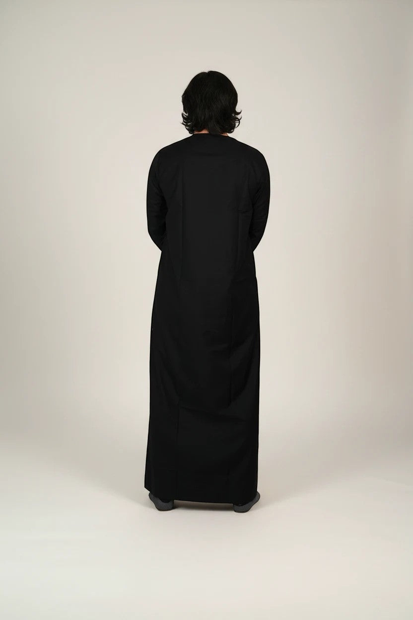 Khayr Thobes traditional black thobe with gold and black embroidery and tassels. Long sleeves, flowing silhouette.